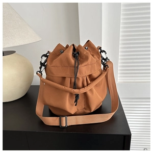 Detail of brown drawstring bucket bag featuring pleated nylon fabric and adjustable strap