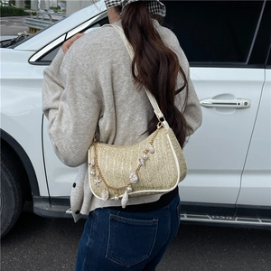 Straw underarm bag with seashell pearls chain shown in an outdoor lifestyle setting