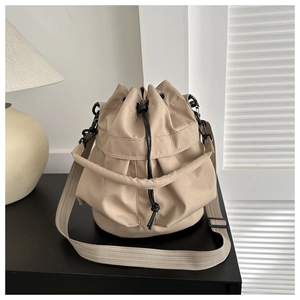 Detail of a beige drawstring bucket bag with a large zipper pocket on a sleek black table