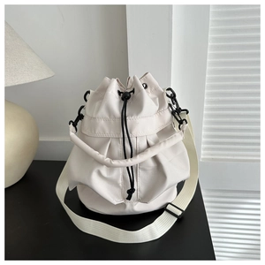 Detail of a cream bucket bag showing drawstring closure and metallic buckle on black surface