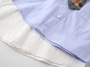 Detail of baby boy shirt showing blue layered hem, white inner fabric, and button design