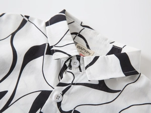 Détail du col d'une chemise enfant avec motifs vagues noires et boutons blancs