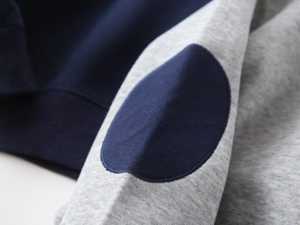 Detailed macro view of grey knit sweatshirt sleeve with navy blue elbow patch detail