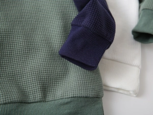 Detailed macro view of waffle knit fabric texture and ribbed cuffs on boys' sweatshirts