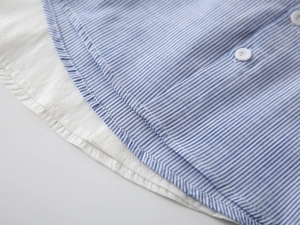 Detail eines blau gestreiften Jungen-Baumwollhemds mit weißen Knöpfen und sauberem Saum