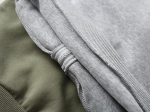 Detail of color-block hooded jacket with olive green and grey fabric and zipper