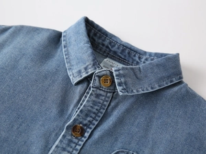 Close-up of boys denim shirt collar with amber buttons and washed blue fabric texture
