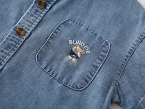 Detail of boys' denim shirt featuring bear embroidery and premium brown buttons