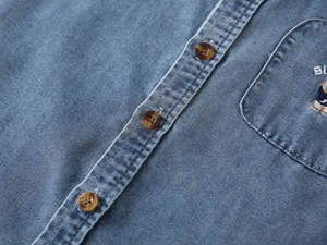 Detail of blue denim shirt featuring amber buttons and bear embroidery on the pocket