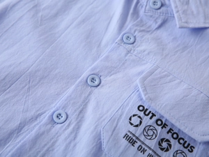 Detail of light blue wrinkled cotton shirt with 'OUT OF FOCUS' print on chest pocket