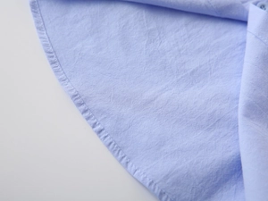 Detailed view of the light blue shirt's curved hem with precise single needle stitching
