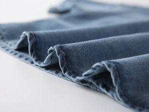 Close-up of blue denim shirt fabric showing detailed twill texture and neat stitching