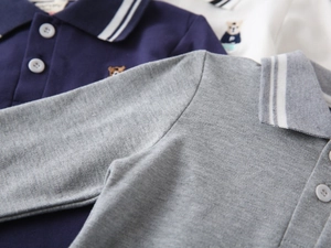 Detail of boys polo shirts showing striped collar and bear embroidery on pique fabric