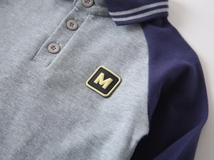 Dettaglio della polo da bambino con tessuto testurizzato, abbottonatura e patch con logo M