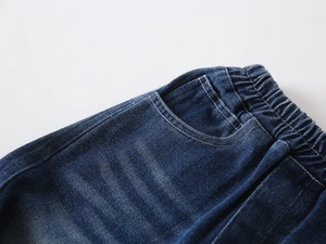 Detail of boys' dark blue denim pants showing elastic waist, pocket stitching, and texture