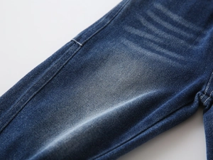 Detailed macro view of dark blue denim fabric with washed whiskers and white stitching