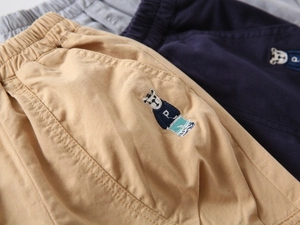 Detail of embroidered bear patches on boys' cotton shorts in khaki and navy blue