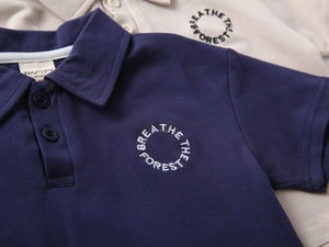 Detail of pique fabric polo shirt with embroidered forest circle logo and button collar