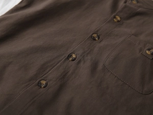 Detail of dark brown cotton-linen shirt texture with amber buttons and front pocket