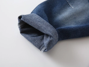 Detail of dark blue denim hem with white overlock stitching on children's jeans
