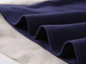 Macro shot of navy blue polo hem showing precise double-needle stitching and fabric texture