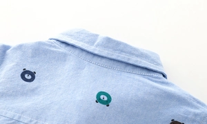 Detail of colorful bear embroidery on the back shoulder of a blue oxford shirt