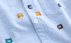Detail of light blue oxford cotton shirt with colorful bear prints and white buttons