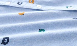 Close-up of light blue Oxford shirt fabric with colorful bear prints and white buttons