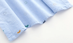 Close-up of baby boy oxford shirt stitching with colorful bear pattern on light blue cotton