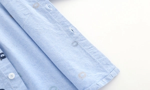 Detailed macro view of light blue oxford shirt fabric with bear pattern and buttons