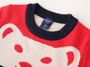 Close-up of red knit sweater featuring cartoon bear pattern and detailed brand neck label