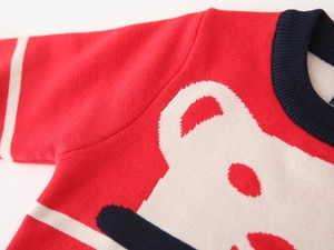 Detail of red knitted toddler sweater showing ribbed crew neck and bear jacquard pattern