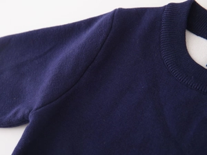 Macro detail of the ribbed crew neck and shoulder stitching on a navy knit sweater for boys