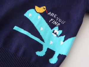 Detail of navy blue knit sweater featuring intarsia dinosaur pattern and ribbed hem