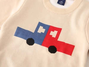 Detail of boys knit sweater featuring a blue and red car pattern on soft cream fabric