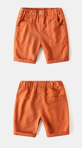 Detail of orange cotton boys shorts featuring elastic waist and wood button detail