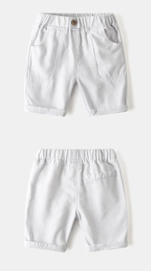 Detail of white cotton boy shorts featuring elastic waist, wooden button and cargo pockets