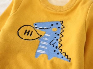 Detail of yellow knit sweater featuring blue cartoon dinosaur pattern and Hi text bubble