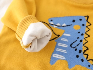 Detail of yellow knit kids sweater showing dinosaur pattern and ribbed cuffs with lining