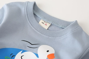 Detail of baby sweatshirt featuring ribbed crew neck and cartoon duck print on blue fabric