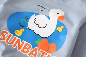 Detail of light blue kid's sweatshirt featuring a cartoon sunbath duck print and ribbed neck