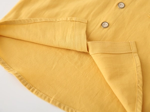 Macro detail of ginger yellow cotton shirt featuring a curved hem and buttoned placket