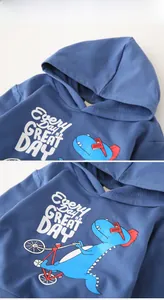 Detail of kids hooded sweatshirt featuring a blue dinosaur riding a bike and graphic text