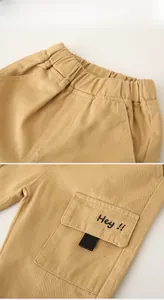 Detail of khaki kids trousers showing elastic waist and cargo pocket with embroidery