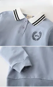 Detail of light blue boys' polo sweatshirt featuring white collar and leaf embroidery