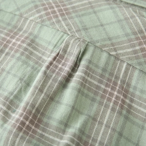Detailed macro view of green and brown plaid fabric texture and fine stitching on shirt