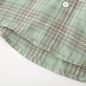 Close-up of green plaid cotton fabric texture and white resin button on a shirt hem