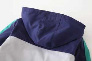 Detail of color-block hooded jacket with navy, white, and green windproof fabric