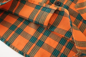 Détail d'une chemise à carreaux orange montrant la texture du coton, bouton et couture