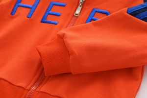 Detail von orangefarbenem Kapuzenpullover mit HERO-Stickerei und Metallreißverschluss